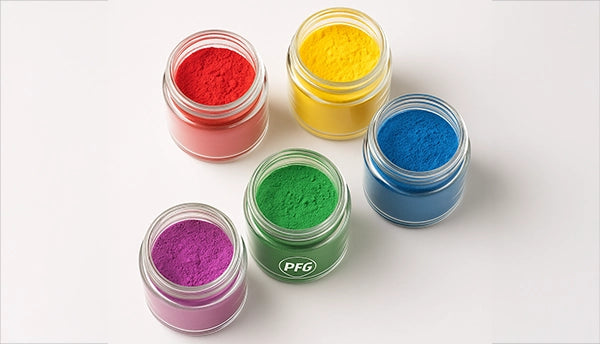 Overhead view of five glass beakers filled with red, yellow, green, blue, and purple food color powders on a white background, showcasing PFG’s precise colorant blending.