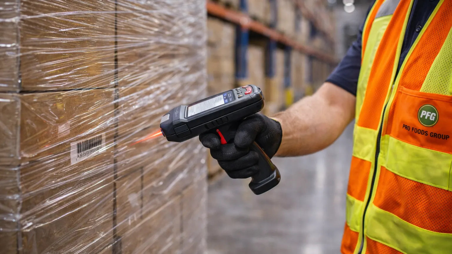 Close-up of worker scanning stretch-wrapped pallet of cardboard boxes in organized warehouse storage facility